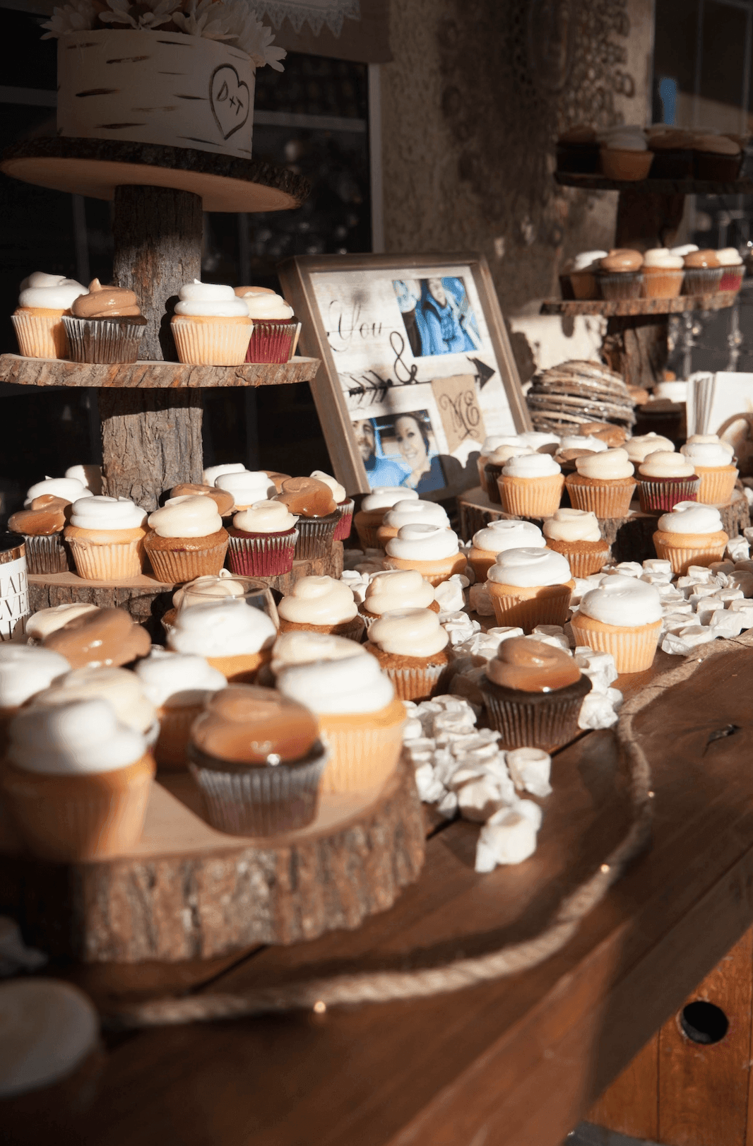 Rustic dessert table with cupcakes on wooden stands and framed photos in the background.